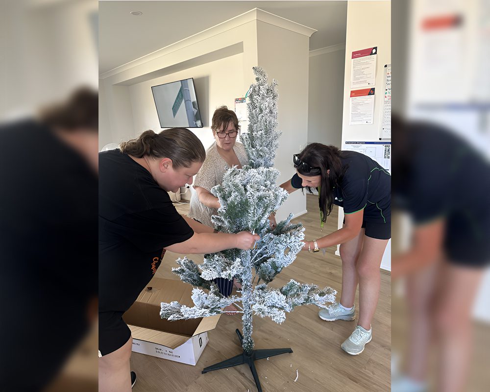 Three women are putting paper on a christmas tree.