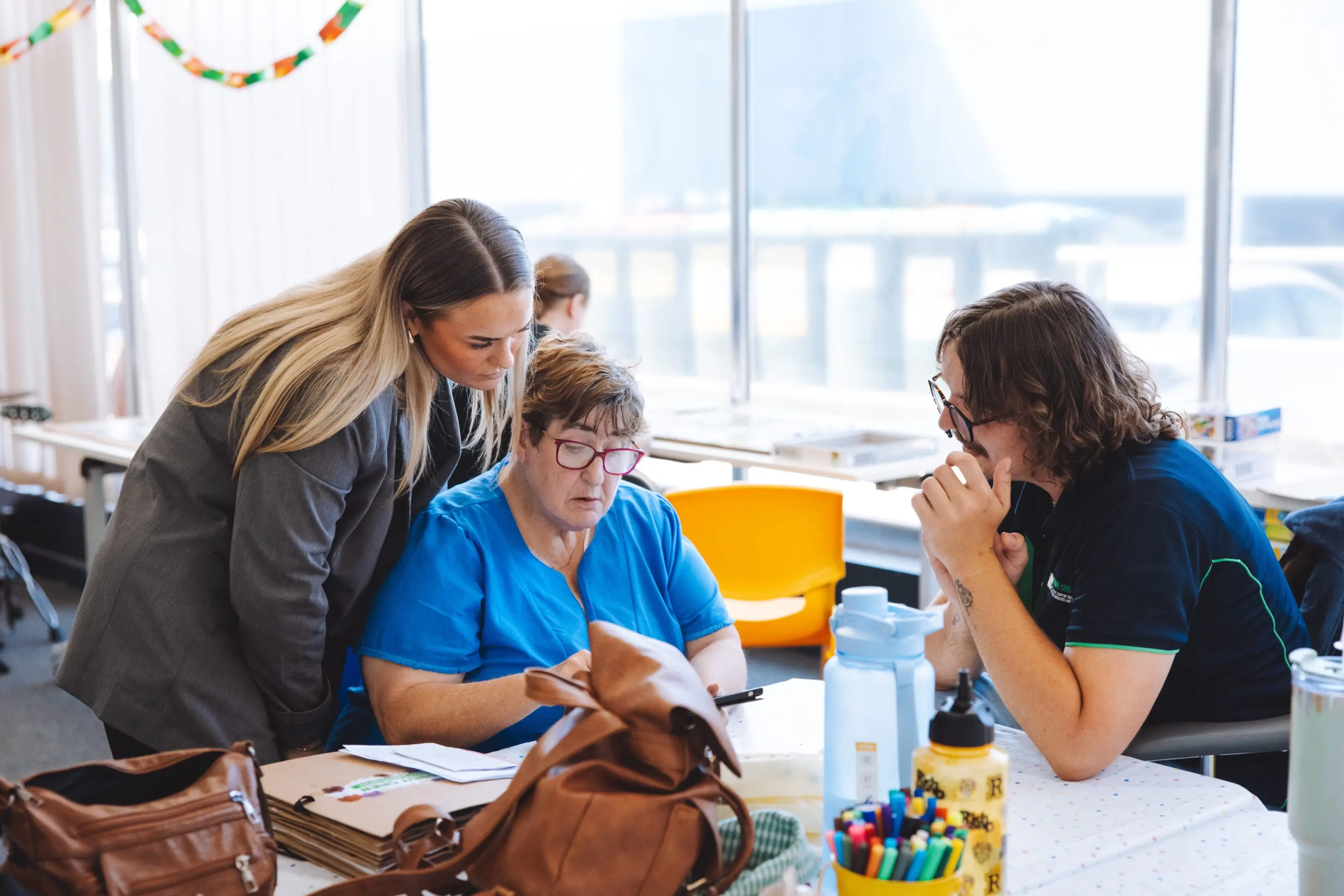 Three women are sitting at a table and one is looking at papers.