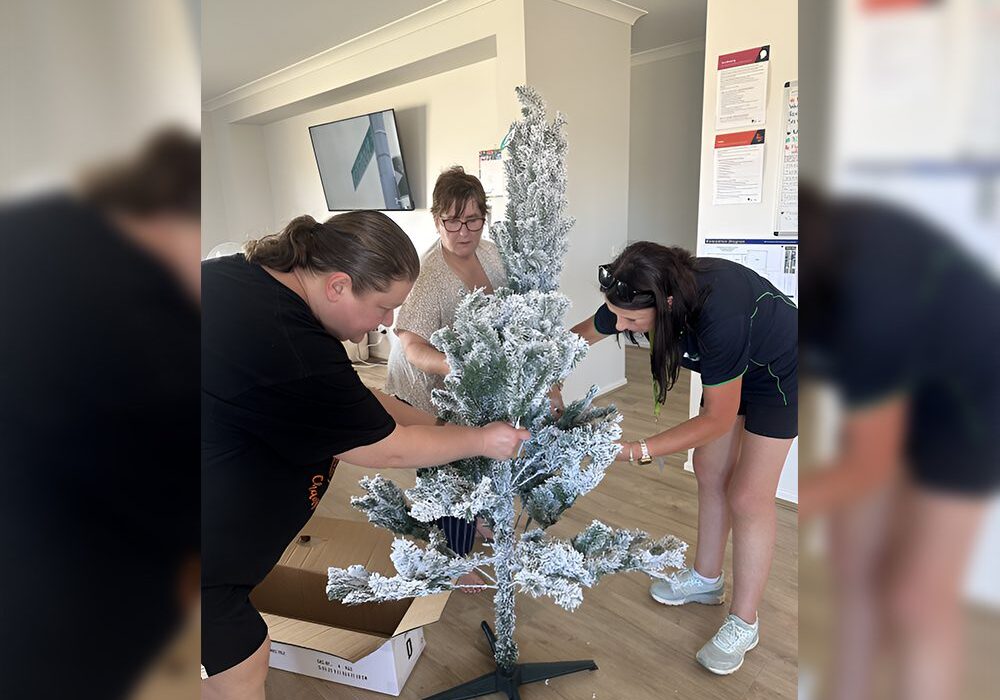 Three women are putting paper on a christmas tree.